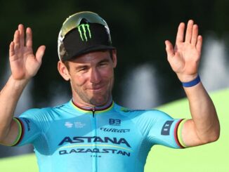 Mark Cavendish in a blue top with his hands in the air.