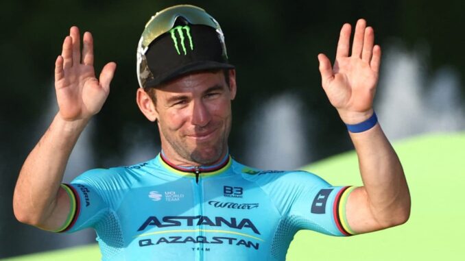 Mark Cavendish in a blue top with his hands in the air.